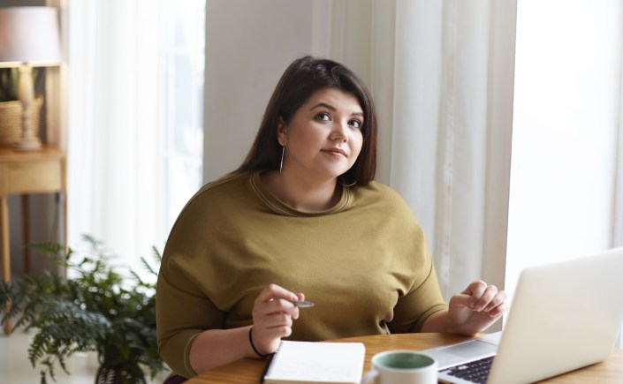 photo d'une jeune femme face à un ordinateur en train de réfléchir à ce qu'elle va écrire